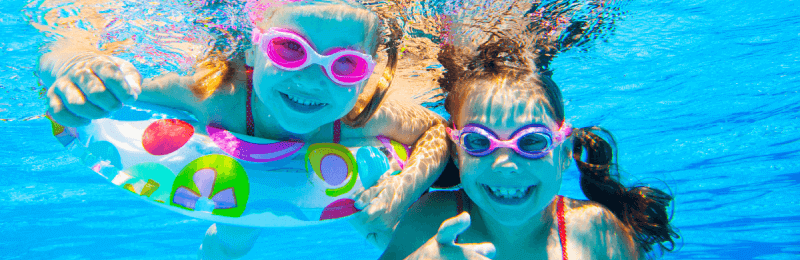 Two happy girls in goggles swimming under water.